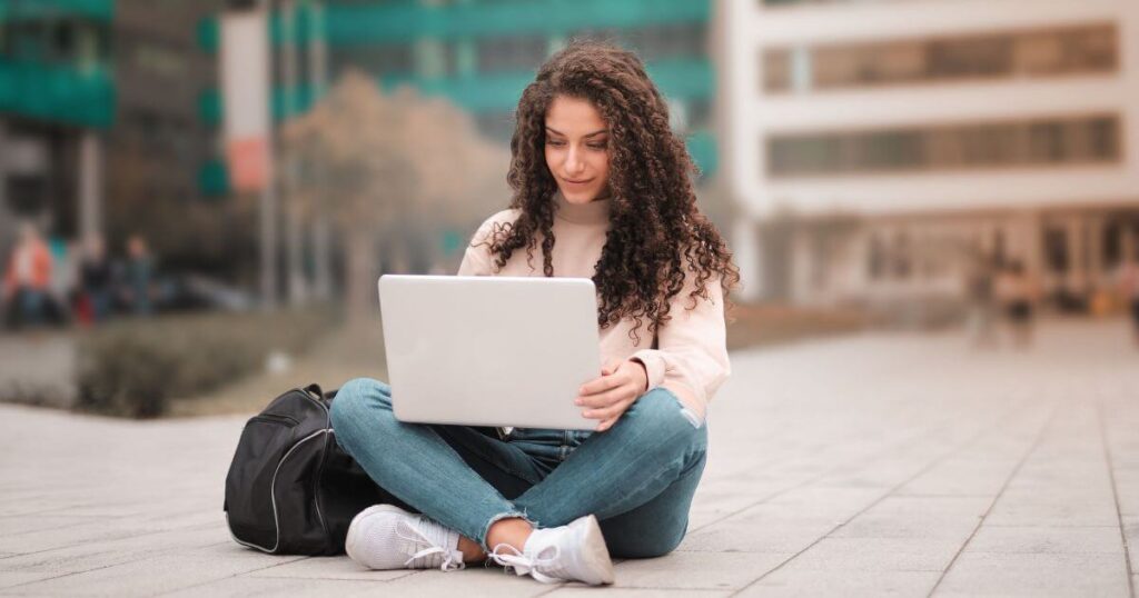 woman-in-pink-sweater-and-black-backpack-using-laptop